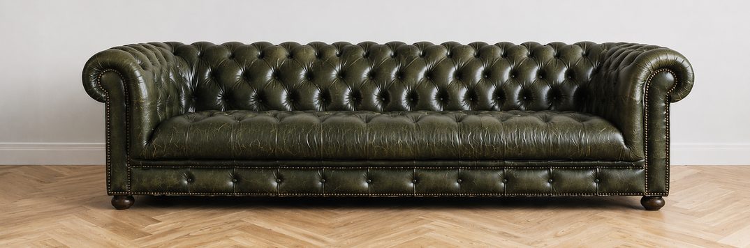 A green tufted leather Chesterfield sofa on a herringbone wood floor in a bright, minimal room